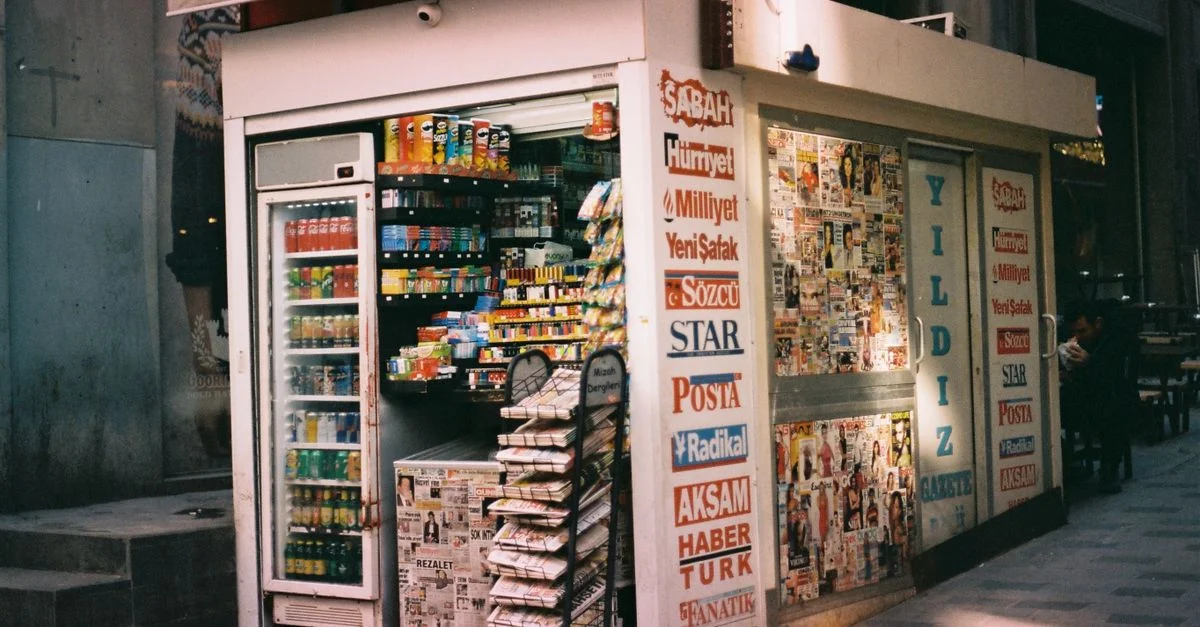Vue de rue d'un kiosque urbain vendant des magazines, des boissons et des collations.