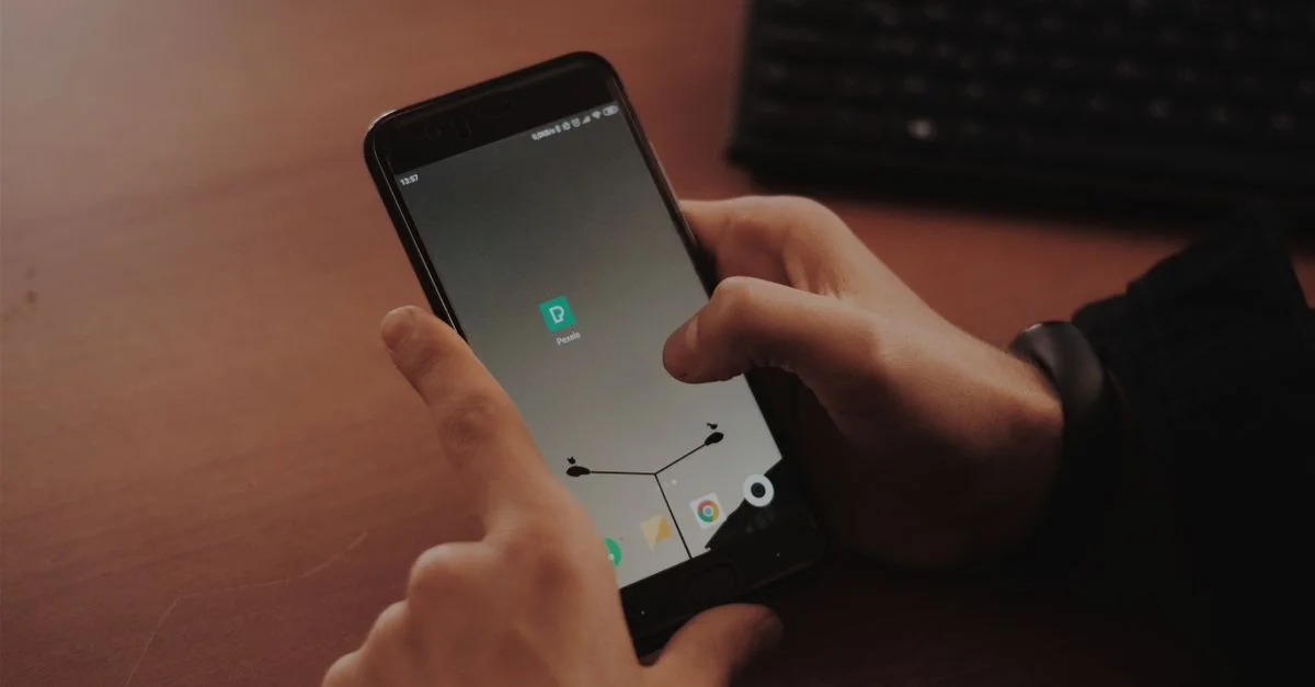 Des mains interagissant avec un smartphone sur un bureau en bois, mettant en avant la technologie moderne.