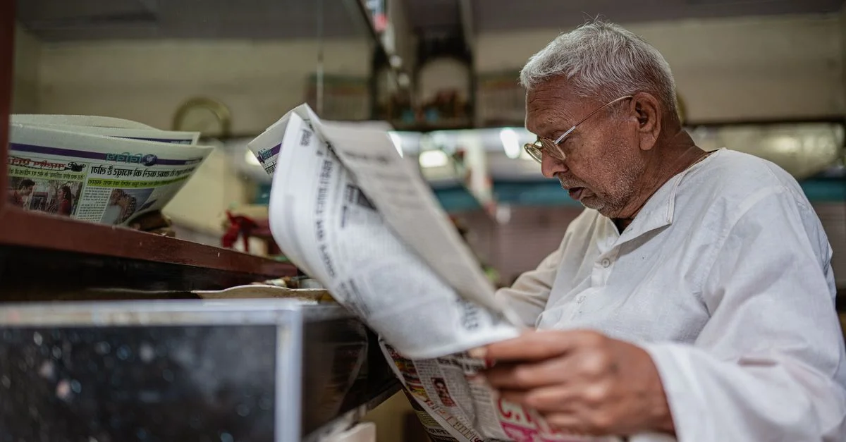 Un homme âgé en tenue traditionnelle lit un journal à l'intérieur d'un magasin à Varanasi, en Inde.