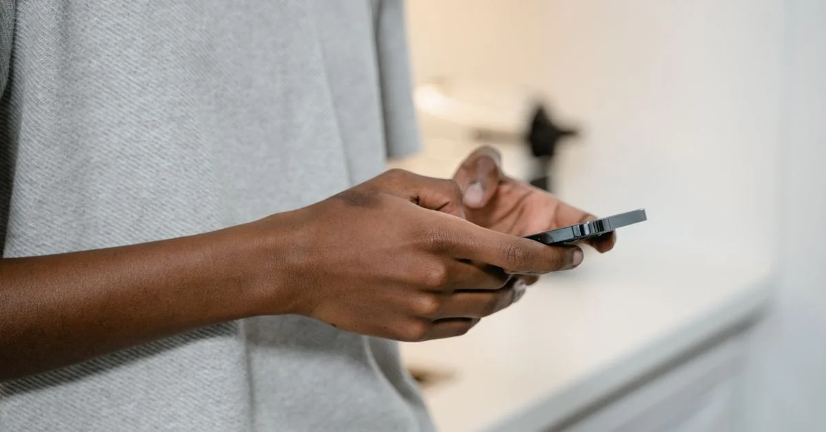 Une personne envoyant des messages sur un smartphone à l'intérieur, montrant les mains et l'appareil en gros plan.