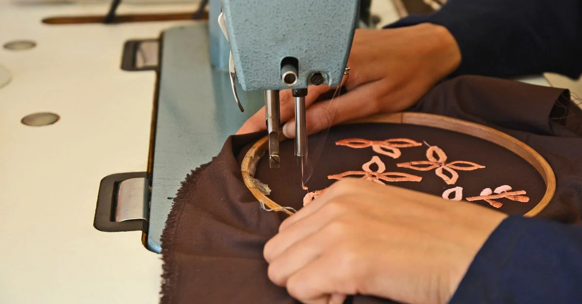 Gros plan sur des mains brodant du tissu à l'aide d'une machine dans un atelier artisanal de Fès.