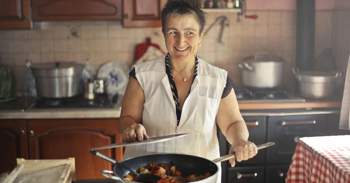 Une femme joyeuse préparant un repas dans une cuisine rustique et chaleureuse.