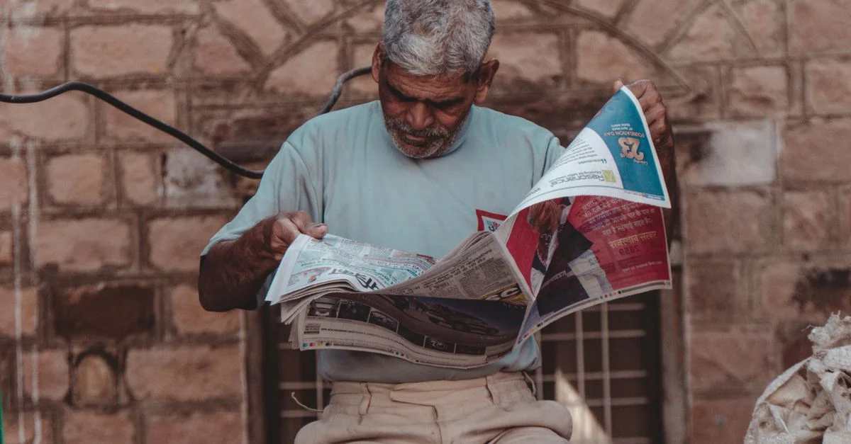Homme senior aux cheveux gris assis dehors, lisant un journal à Mumbai, Inde.