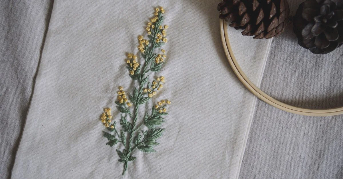 Tissu artistique présentant une broderie florale détaillée accompagnée de pommes de pin.