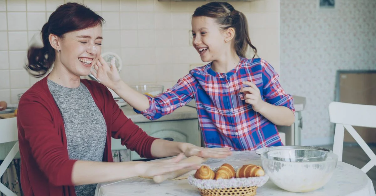 Une mère et sa fille rient et cuisinent ensemble dans une cuisine chaleureuse.
